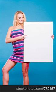 Presenting advertisement concept. Happy positive blonde woman wearing colorful short dress holding blank white board. Happy positive blonde woman holding blank white board