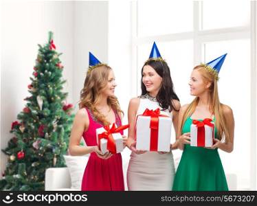presents, holidays, people and celebration concept - smiling women in party caps with gift boxes over living room and christmas tree background