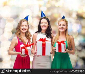 presents, holidays, people and celebration concept - smiling women in party caps with gift boxes over lights background