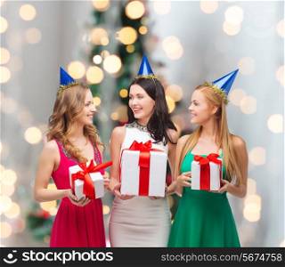 presents, holidays, people and celebration concept - smiling women in party caps with gift boxes over christmas tree lights background