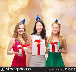 presents, holidays, people and celebration concept - smiling women in party caps with gift boxes over beige lights background