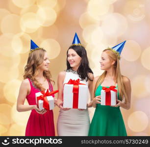 presents, holidays, people and celebration concept - smiling women in party caps with gift boxes over beige lights background