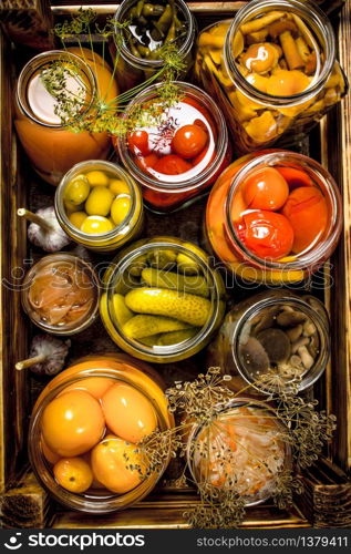 Preserves mushrooms and vegetables in a box. On a wooden background.. Preserves mushrooms and vegetables in a box.