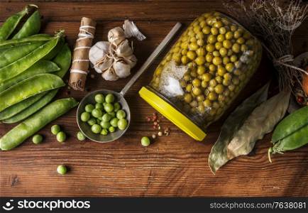 Preserving of garden vegetables. Green peas canning in jar on wooden background with ingredients. Top view. Healthy clean organic homemade preserve concept