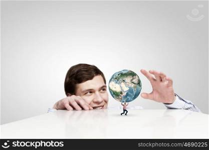Pressure of responsibility. Businessman looking from under table at man lifting Earth planet. Elements of this image are furnished by NASA