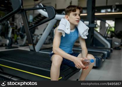 Preteen boy rest after hard training workout on treadmill at gym. Sport for kid to develop strength and endurance concept. Preteen boy rest after hard training workout on treadmill at gym