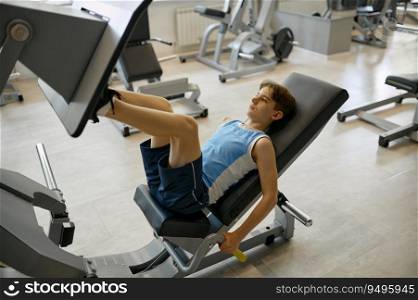 Preteen boy training legs on sports equipment at gym. Young male athlete pushing slab with feet to be strong and health. Preteen boy training legs on sports equipment at gym