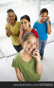 Preteen girls of mutiple ethnicities talking on cell phones and looking at viewer.