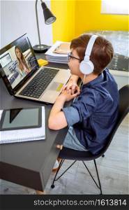 Preteen with headphones receiving class at home with laptop from his bedroom. Home schooling concept