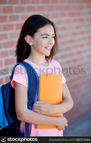 Preteenager girl next to a red brick wall with the backpack and books
