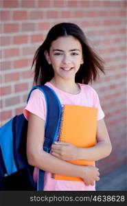 Preteenager girl next to a red brick wall with the backpack and books