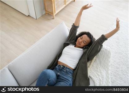 Pretty african american teenage girl lies on couch at home. Lazy weekend morning. Young woman is stretching and smiling. Girl is chilling in sunday morning. Comfort and relaxing at home concept.. Pretty african american teenage girl lies on couch at home. Relaxing in lazy weekend morning.
