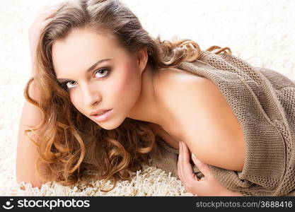 pretty and attractive young brunette in a warm brown sweater laying down on a white carpet, she looks in to the lens with sexy expression, her right hand is near the face and the left hand is on chest