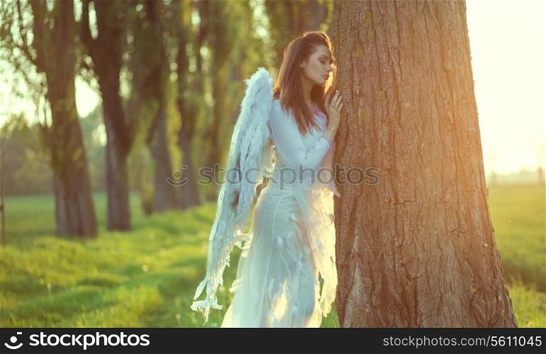 Pretty angel leaning against the huge tree