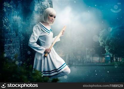 Pretty anime style blonde girl with baseball bat. Cosplay woman, asian culture, doll with wooden bit in cold tones, night city park on background