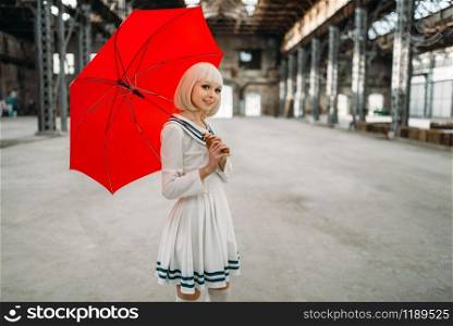 Pretty anime style blonde girl with red umbrella. Cosplay fashion, asian culture, doll in dress, cute woman with makeup in the factory shop