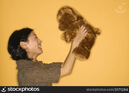 Pretty Asian mid adult woman holding brown teddy bear and smiling.