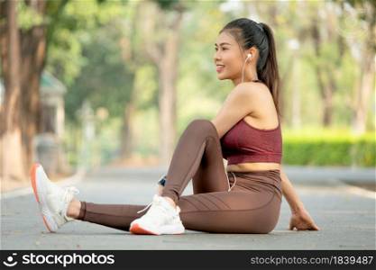 Pretty Asian woman with sportswear sit on road floor in park or garden do leg stretching and she also look to her right side.