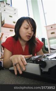 Pretty Asian young woman lying on floor in red robe typing on typewriter.