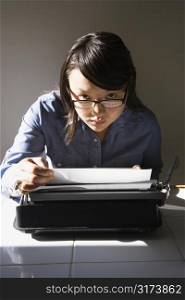 Pretty Asian young woman with typewriter making eye contact over glasses.