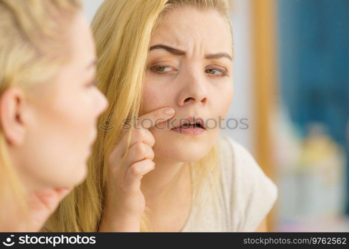 Pretty attractive young adult woman looking at herself in bathroom mirror thinking about her look checking skin condition. Woman looking at her skin in mirror