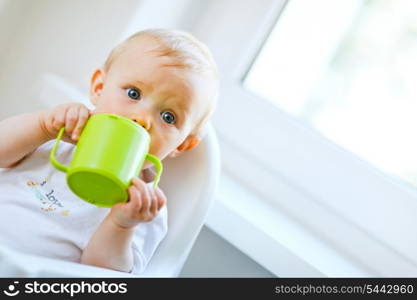 Pretty baby sitting in chair and drinking from baby cup &#xA;