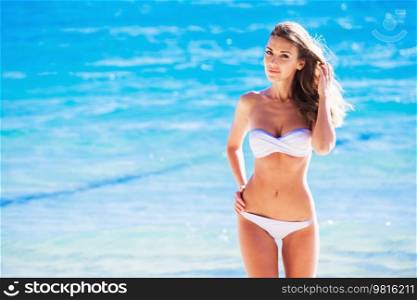 Pretty beautiful woman in white swimwear bikini posing in blue sea water. Woman in bikini posing in blue sea water