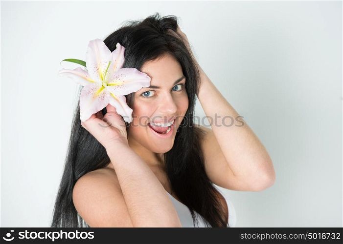 Pretty beautiful woman with healthy skin and pink lily in her hairs laughing and looking at camera