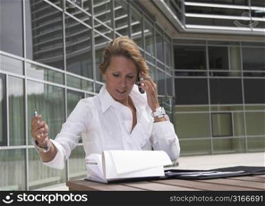 Pretty blond businesswoman sitting outdoors at table in front of office building, talking on the phone