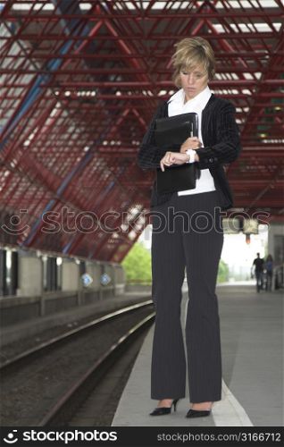 Pretty blond businesswoman standing on the trainstation checking her watch to see when the next train will arrive