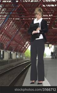 Pretty blond businesswoman standing on the trainstation checking her watch to see when the next train will arrive