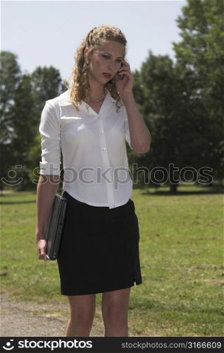 Pretty blond businesswoman talking on the phone while on her lunchbreak in the park