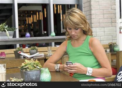 Pretty blond girl sitting on a terrace sending text messages to her friends