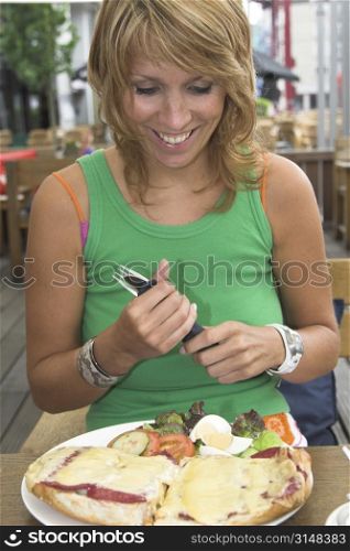 Pretty blond girl sitting outdoors on a terrace and looking very happy with her food that just arrived