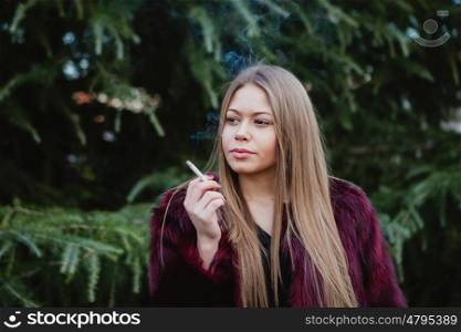 Pretty blond girl with long hair smoking in the park