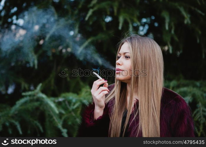 Pretty blond girl with long hair smoking in the park