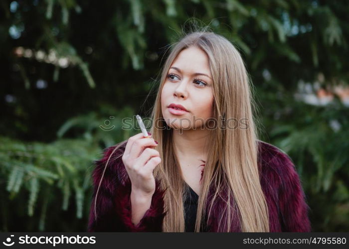 Pretty blond girl with long hair smoking in the park