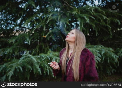 Pretty blond girl with long hair smoking in the park