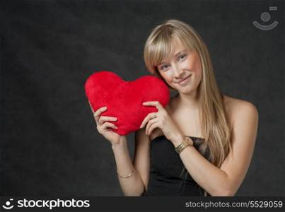 Pretty blond haired women with her heart in hands. Beautiful young woman holding a heart shaped red pillow and smiling