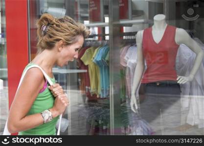 Pretty blond woman looking shocked in the window of a clothing store