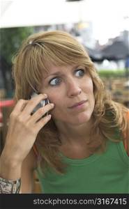 pretty blond woman looking shocked while listening to the phone