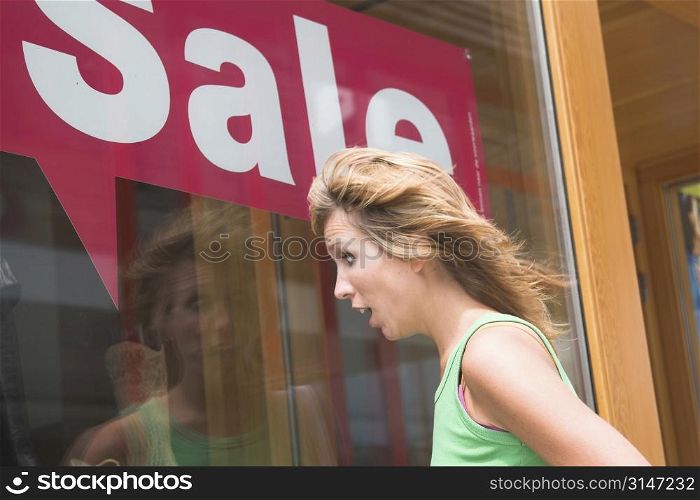 Pretty blond woman looking totally shocked when looking in the window of the shoestore with summersale