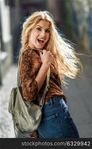 Pretty blond woman, model of fashion, smiling with flying hair. Beautiful girl wearing shirt and blue jeans carrying a bag