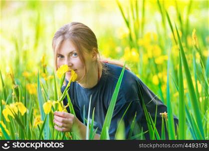 Pretty blond woman smells yellow flowers on the sunny green field