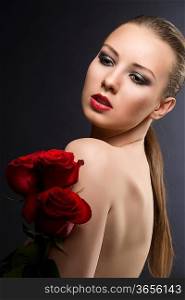 pretty blonde girl&acute;s low key portrait with three red roses, her body is turned in profile, her face is turned of three quarters and looks down at right