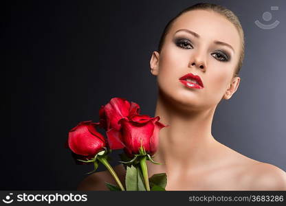 pretty blonde girl&acute;s low key portrait with three red roses, she is in front of the camera with head slightly folded at right and looks in to the lens