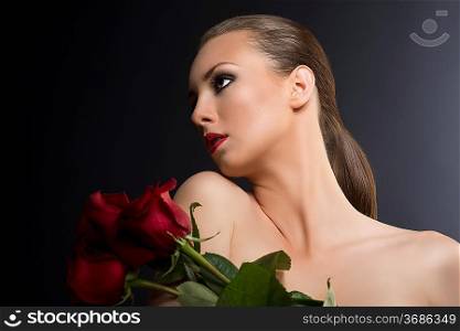 pretty blonde girl&acute;s low key portrait with three red roses, she is in front of the camera, her face is turned in profile at right and tilted back