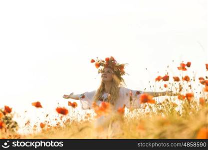 Pretty blonde girl in a dress with a pattern poppy and with a wreath on his head enjoying in a field with poppies. Girl in a poppy field