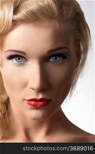 pretty blonde girl in close-up beauty portrait with cute make-up, red lipstick. Looks in camera on gray background