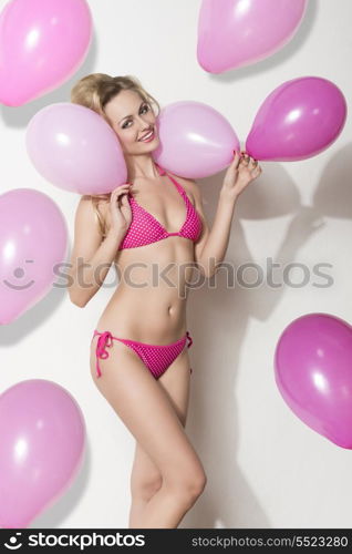pretty blonde girl with bikini taking pink balloons in the hands and smiling